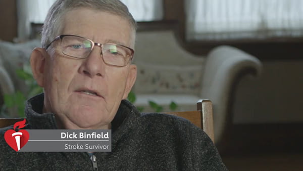 A video screen shot of stroke survivor, Dick Binfield, a senior white man with glasses sitting in a chair in a home setting