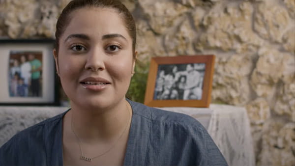 Una captura de video de Noelia, sobreviviente de ataque o derrame cerebral, frente a fotografías familiares enmarcadas en la repisa de una chimenea