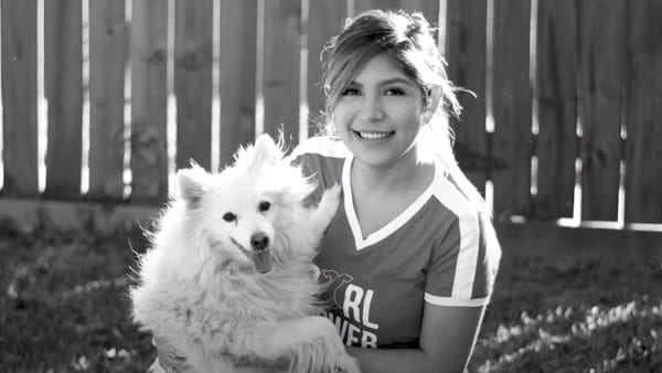 Una fotografía en blanco y negro de Steffany Quintana, sobreviviente de derrame cerebral, posando con su perro frente a un cerco