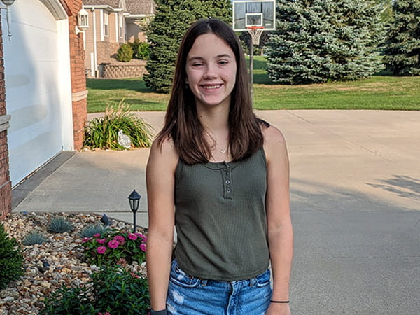 A smiling Reegan Lueken is standing in the driveway of her home.