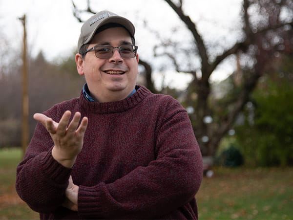 Rick Hoeg is smiling and posing with his hand out in an outdoor setting.