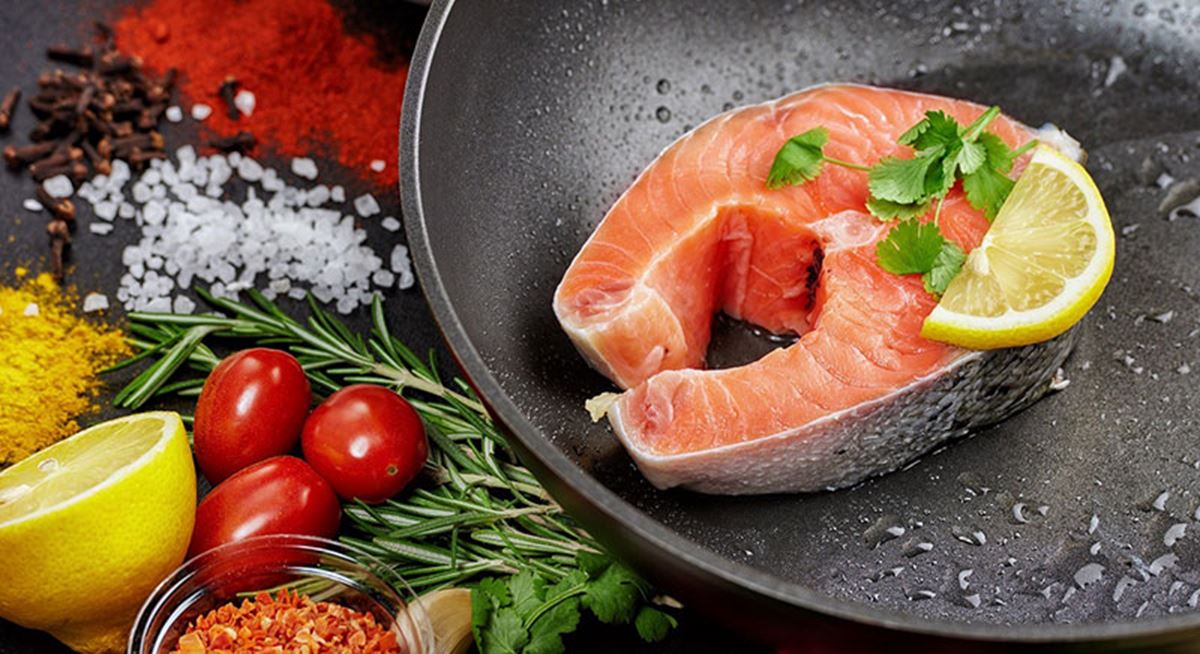 Salmon steak in a cast iron skillet surrounded by vegetables 