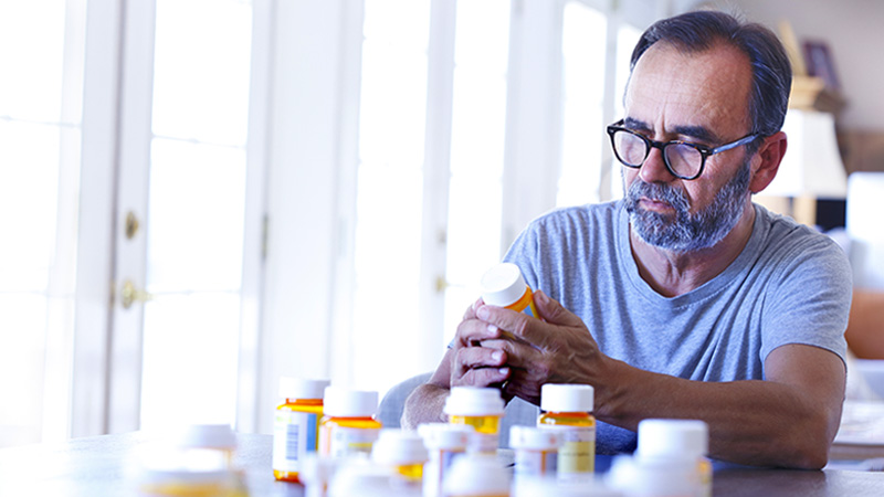 An older Latino man is sitting at a table sorting through prescription medications. An older Latino man is sitting at a table sorting through prescription medications.