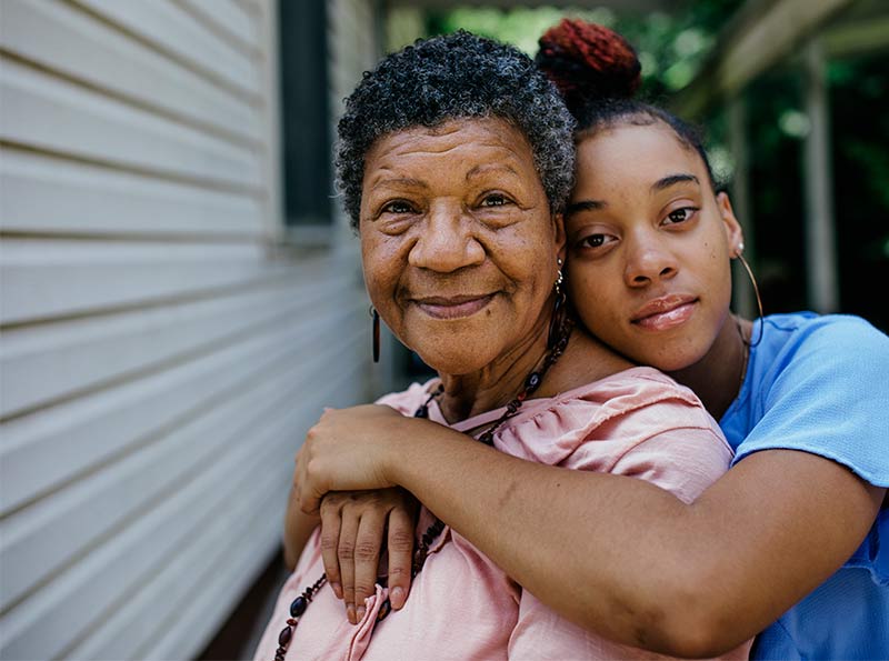 A teenaged Black girl with her arms wrapped around her smiling grandmother A teenaged Black girl with her arms wrapped around her smiling grandmother