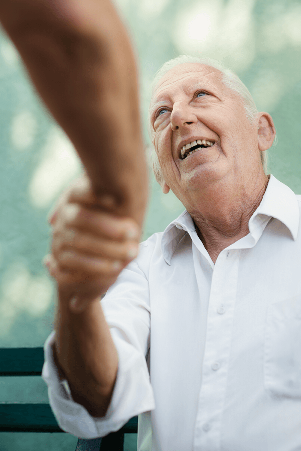 A senior man is sitting on a bench and shaking hands with someone