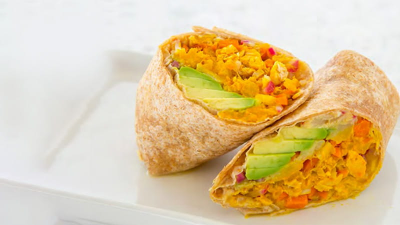 A tuna wrap with avocado is sliced in half and arranged on a plate. A tuna wrap with avocado is sliced in half and arranged on a plate.