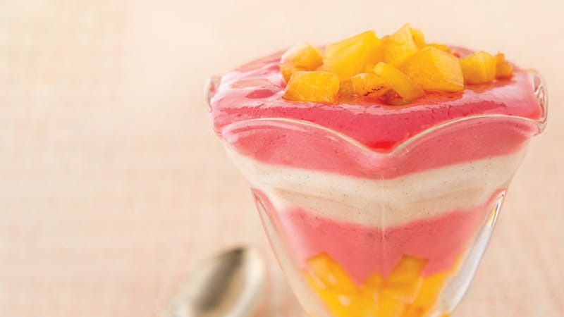a parfait glass containing pink, white and yellow layers of yogurt and fruit a parfait glass containing pink, white and yellow layers of yogurt and fruit