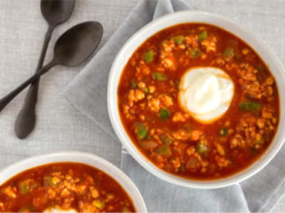 an aerial view of two bowls of chili with a dollop of yogurt and spoons arranged on grey table linens an aerial view of two bowls of chili with a dollop of yogurt and spoons arranged on grey table linens