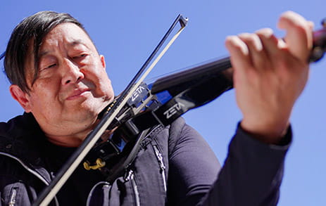 Stroke survivor, Dave, is playing a violin with a blue sky in the background.