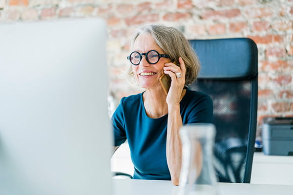 A senior woman is sitting at her desk and talking on a mobile phone. A senior woman is sitting at her desk and talking on a mobile phone.
