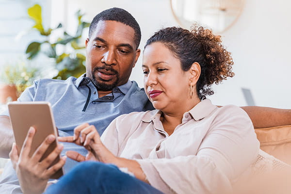 Un hombre y mujer adultos sentados en un sofá mirando juntos su tableta digital. Un hombre y mujer adultos sentados en un sofá mirando juntos su tableta digital.