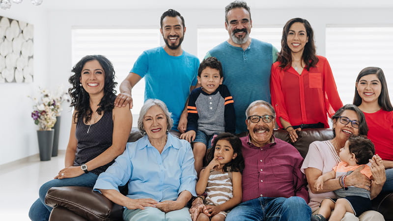 A multigenerational Hispanic family sitting around a sofa and posing for the camera A multigenerational Hispanic family sitting around a sofa and posing for the camera