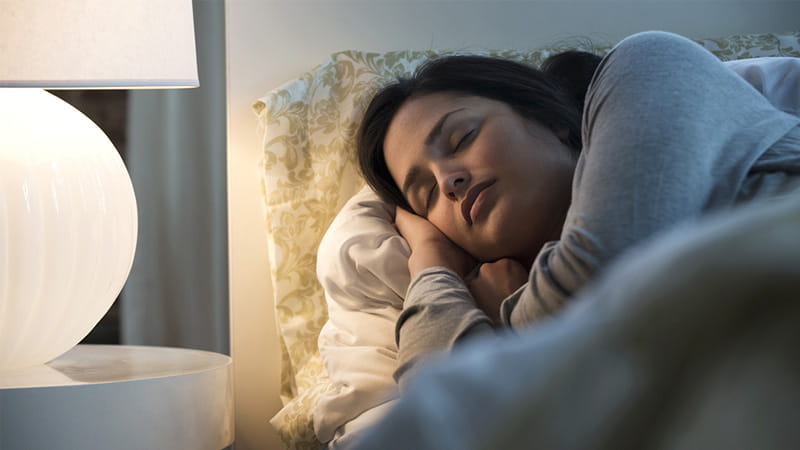 Una mujer de origen hispano/latino iluminada por una lámpara duerme en una cama. Una mujer de origen hispano/latino iluminada por una lámpara duerme en una cama.