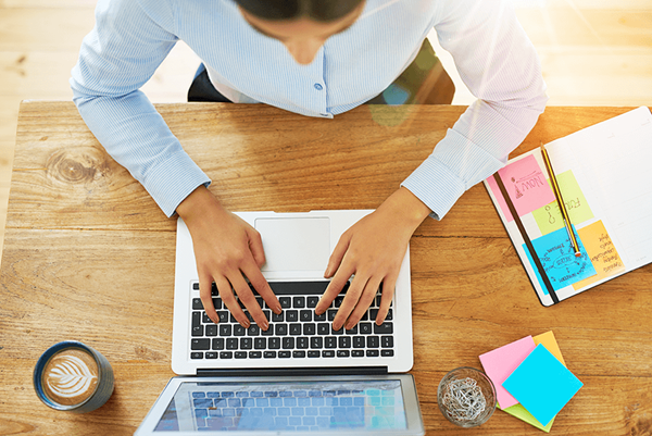 From an aerial view, a woman is sitting at a desk typing on a laptop. top down view of woman typing on laptop